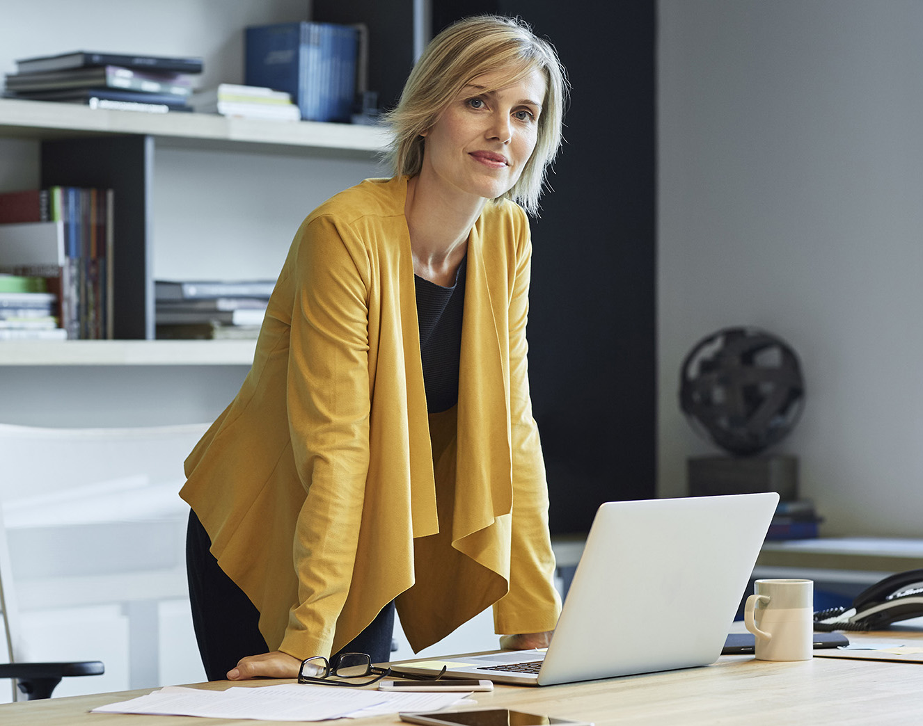 Confident businesswoman leaning on desk